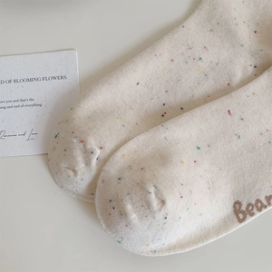 Detailed knit texture of beige crew socks featuring colorful flecked yarn and Bear embroidery