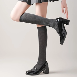 Detail view of dark grey knee-high socks with ribbed texture and black patent leather shoes