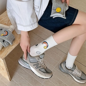 Detail of white cotton socks with rainbow and smiley face print worn with sneakers