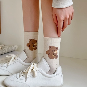 Detailed view of beige speckled socks featuring cute brown bear embroidery and white shoes