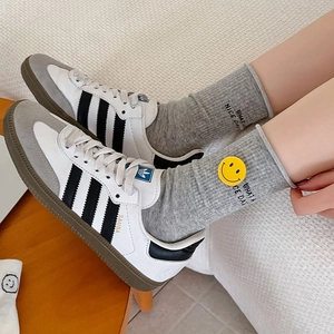 Close-up of white leather sneakers with yellow smiley face socks and embroidered text