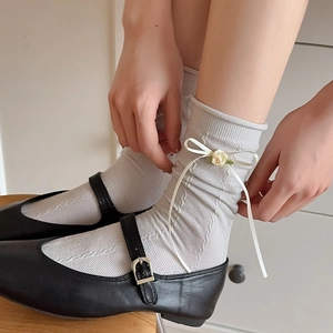 Detail of grey knitted socks with white ribbon bows and yellow 3D rose flower accents