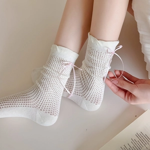 Détail de chaussettes mi-mollet en maille ajourée blanche avec nœuds en ruban de soie rose