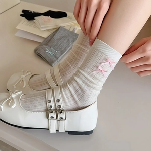 Detail of white ballet-style socks with pink silk bows and vertical ribbed knit texture