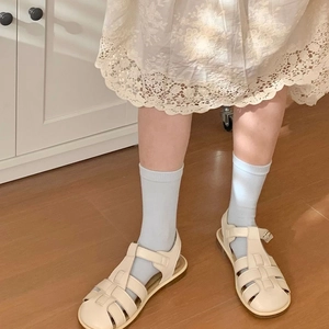 Sandali romani da donna in pelle intrecciata bianco crema su pavimento in legno