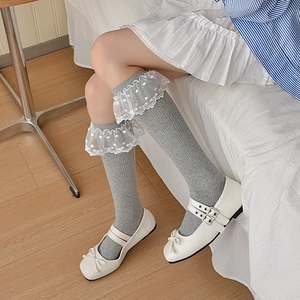 Détail de chaussettes hautes grises avec volants en dentelle blanche et broderies