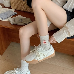 Detailed view of white cotton socks with cherry embroidery paired with thick-sole sneakers