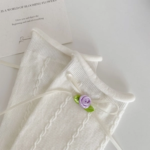 Detail of white cable knit socks featuring small purple silk roses and delicate ribbon bows