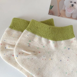 Close-up of confetti dot pattern on cotton socks with green ribbed cuffs and creamy white body