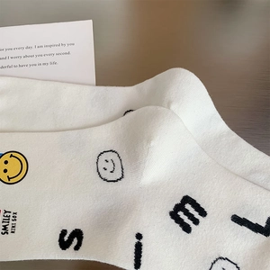 Close-up of white cotton socks featuring a yellow smiley face and Smiley Kiki Sox lettering