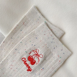 Detail of cream knit sock with colorful speckles and red cherry embroidery detail