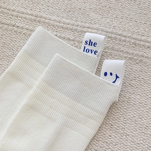Detail of white cotton crew socks with blue she love letter label and ribbed texture