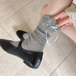 Détail de chaussettes en maille grise avec nœuds blancs et chaussures Mary Jane