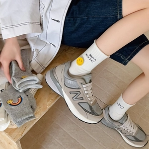 Close-up of white cotton crew socks featuring yellow smile icon and black text slogan