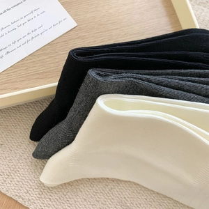 Close-up of ribbed knit crew socks in black, dark grey, and beige on a wooden tray