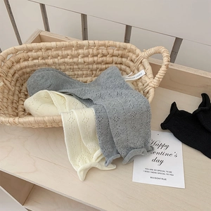 Detailed macro view of hollow knitted baby socks with ruffled edges in a woven basket