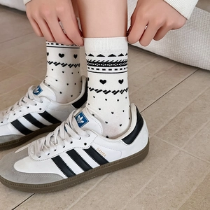 Close-up of white crew socks featuring black heart patterns and fine ribbed cuffs detail