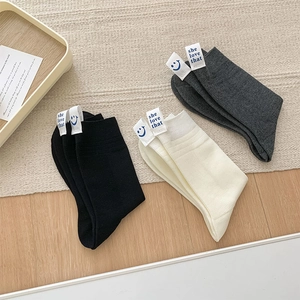 Flat lay of cotton crew socks in black, white, and grey with cute woven smile face labels
