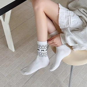 Detail of white cotton crew socks featuring black hearts and bow patterns with a preppy style