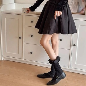 Detail of elegant black pleated skirt styled with mid-calf socks and leather Mary Janes