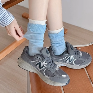 Light blue slouch socks with vertical ribbing paired with grey sneakers on wood floor