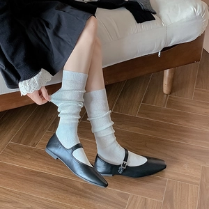 Close-up of ballet-style white shimmering calf socks with black Mary Jane shoes