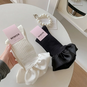 Detailed view of white and black crew socks with elegant satin ruffle lace trim