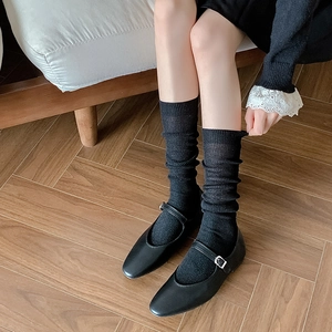 Close-up of black Mary Jane flats with metal buckles and ribbed slouch socks on wood floor