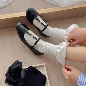 Detail of black patent leather Mary Jane shoes with metallic buckles and ruffled socks