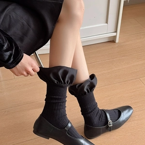 Detail of black ribbed cotton socks with satin ruffle cuffs paired with Mary Jane shoes