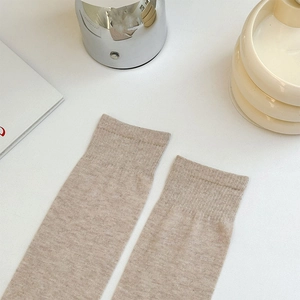 Detail of oat-colored knee-high socks with widened ribbed cuffs and fine knit texture
