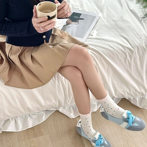 Detalle de calcetines blancos de lunares y zapatillas con lazo azul en cama blanca
