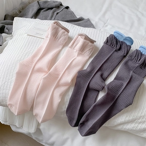 Detail of ribbed knit socks with wavy cuffs in pink and grey on a white bed sheet