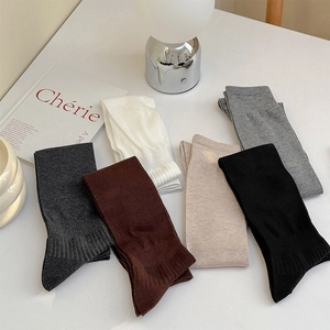 Close-up of ribbed cuffs on six assorted solid color knee-high cotton socks on a white desk