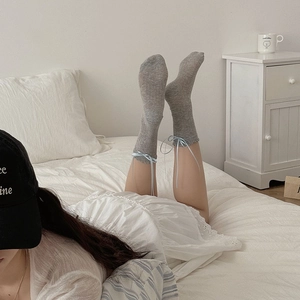Detail of gray knit crew socks featuring a light blue ribbon bow on the cuff in a soft setting