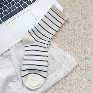 Detail of cream cotton crew socks with navy stripes and red trim in a cozy setting