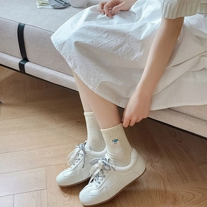 Detail of cream bear embroidery socks with GAT sneakers on wooden flooring