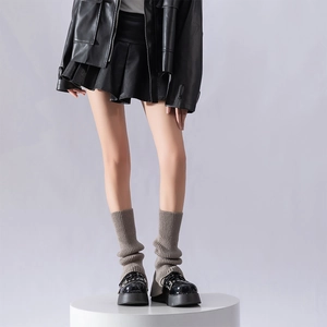 Detail of grey ribbed knit leg warmers styled with black loafers and a pleated skirt