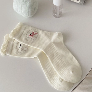 Close-up of cream knit socks featuring ruffled edges, cute puppy embroidery and pink bows