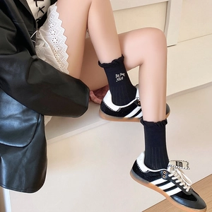 Detail of black crew socks featuring ruffle cuffs and Be Nice bow embroidery