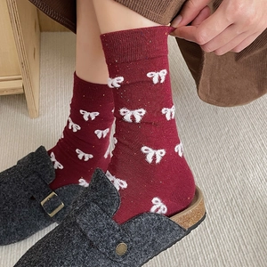 Deep red knit crew socks with white bow patterns paired with felt slippers in home setting