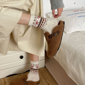 Détail de chaussettes en laine Fair Isle à cœurs rouges et sabots en peluche marron sur lit blanc