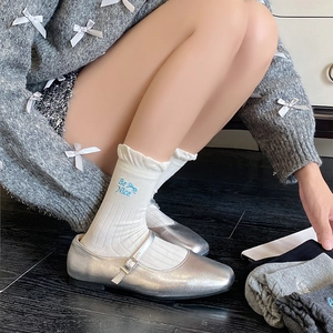 Detail of white ruffle crew socks with blue 'Be Nice' embroidery and silver Mary Jane shoes