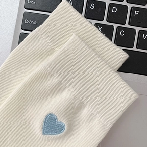 Detailed macro view of cream knitted socks featuring a blue heart embroidery and ribbed cuff