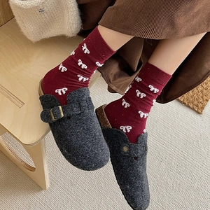 Detail of red striped socks with bow pattern and grey felt mule clogs on wooden bench