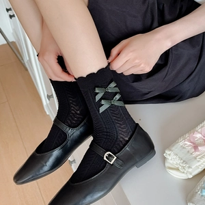 Détail de chaussettes en maille noire avec nœuds à pois verts et chaussures Mary Jane