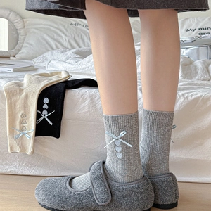 Detail of grey knitted mid-calf socks with blue ribbon bows and heart embroidery accents