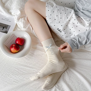 Detailed close-up of cream ribbed crew socks with blue ribbon bows and heart embroidery