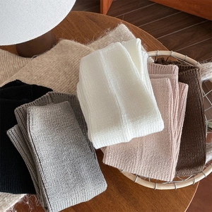 Detailed pile of ribbed knit leg warmers in various neutral colors on a wooden table