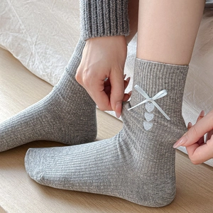 Close-up of grey ribbed cotton socks featuring white satin bows and heart embroidery